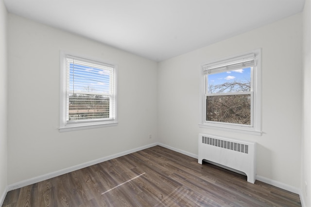 spare room with baseboards, dark wood-type flooring, and radiator heating unit