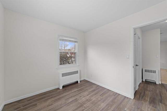 unfurnished room with radiator, wood finished floors, and baseboards