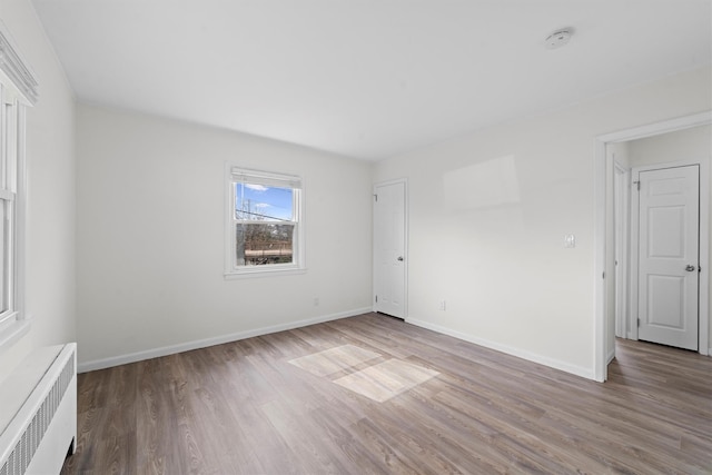 empty room with radiator heating unit, baseboards, and wood finished floors