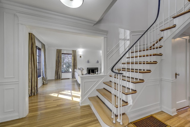 stairs featuring hardwood / wood-style flooring, a decorative wall, a fireplace, and ornamental molding