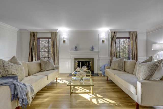 living area featuring crown molding, a decorative wall, a fireplace with flush hearth, and wood finished floors