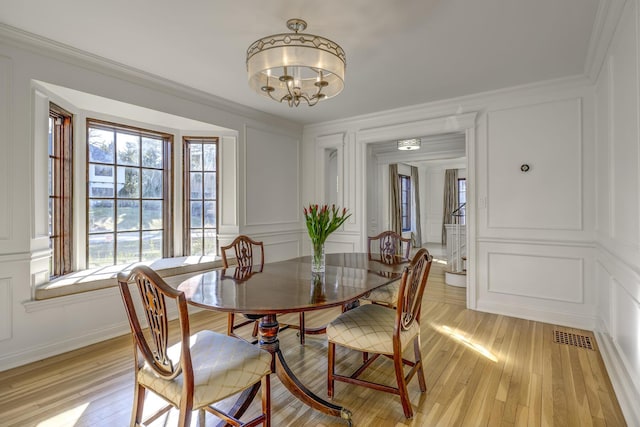 dining space featuring light wood-type flooring, an inviting chandelier, crown molding, and a decorative wall