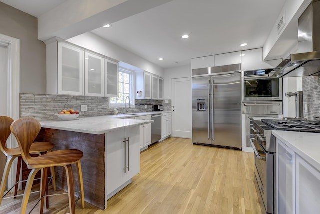 kitchen featuring premium appliances, a peninsula, a breakfast bar area, white cabinets, and wall chimney range hood