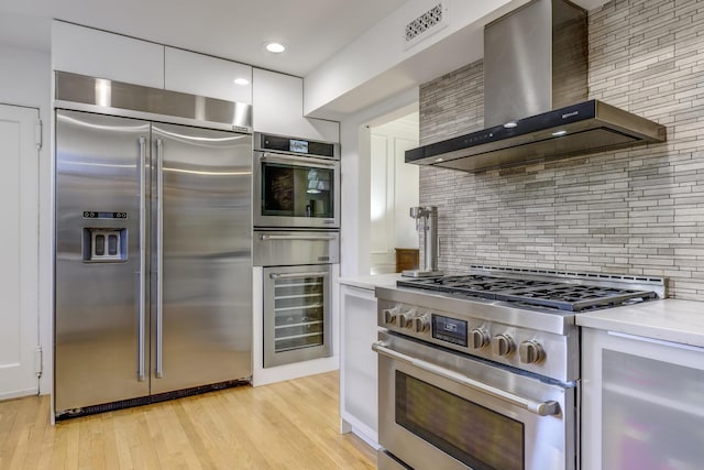 kitchen with visible vents, wall chimney range hood, beverage cooler, high quality appliances, and light wood-style flooring