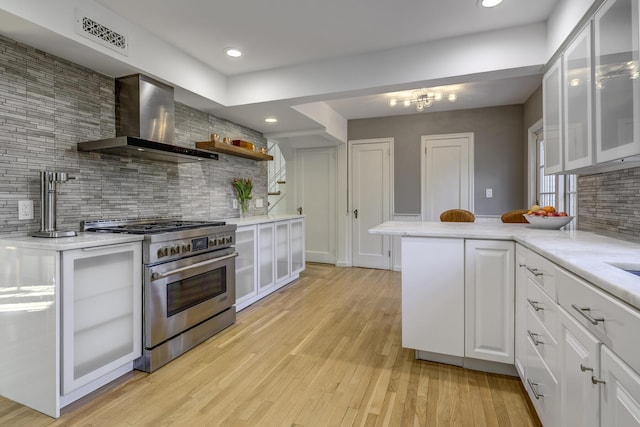 kitchen featuring visible vents, light wood-style flooring, stainless steel stove, white cabinets, and wall chimney range hood