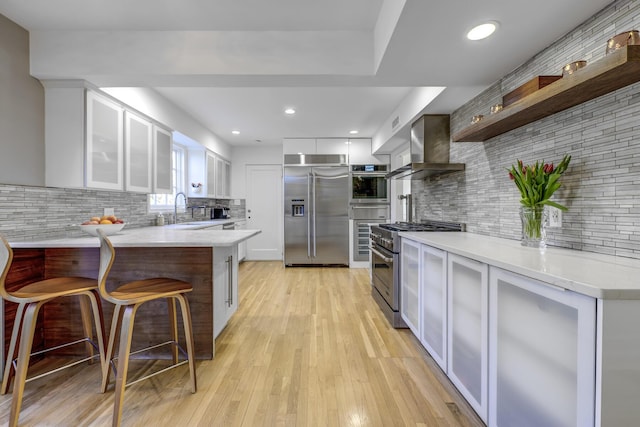 kitchen with a breakfast bar area, high end appliances, open shelves, a peninsula, and wall chimney range hood