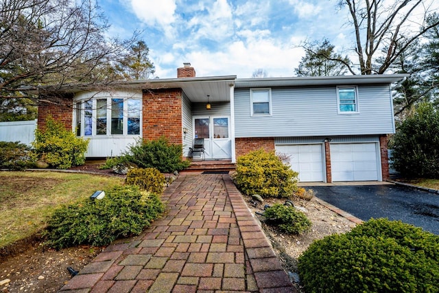 tri-level home featuring aphalt driveway, brick siding, an attached garage, and a chimney