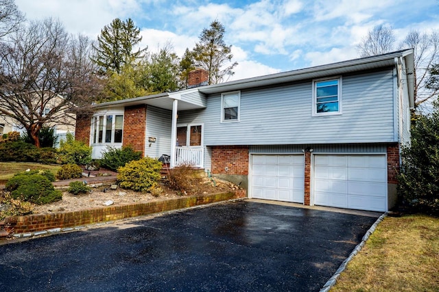 tri-level home featuring aphalt driveway, an attached garage, brick siding, and a chimney