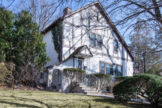 tudor home with stucco siding, a chimney, and a front lawn