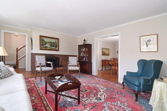 living area with a brick fireplace, crown molding, stairs, and wood finished floors