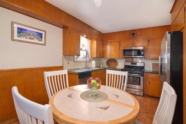 kitchen with brown cabinetry, a wainscoted wall, appliances with stainless steel finishes, and a sink