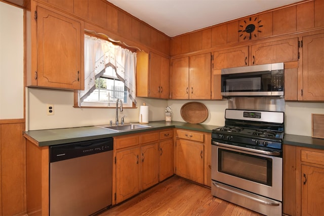 kitchen with dark countertops, light wood-style flooring, appliances with stainless steel finishes, brown cabinets, and a sink