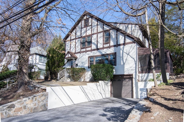 tudor-style house with a garage, driveway, and stucco siding