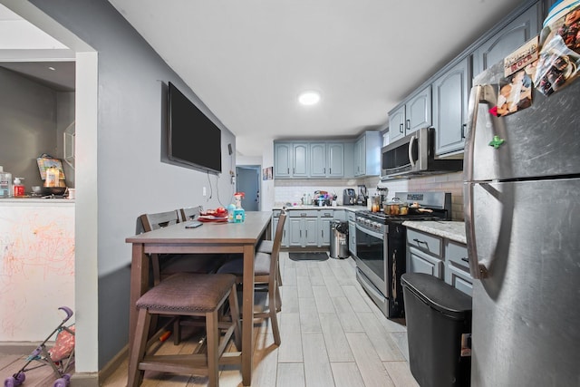 kitchen with gray cabinetry, wood tiled floor, light countertops, decorative backsplash, and stainless steel appliances