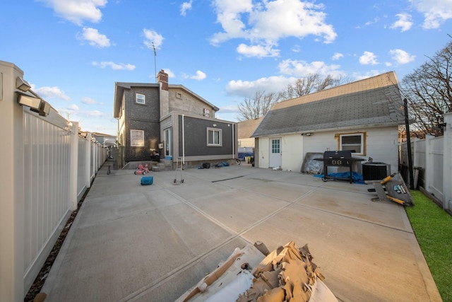 back of house featuring roof with shingles, cooling unit, a chimney, a fenced backyard, and a patio area