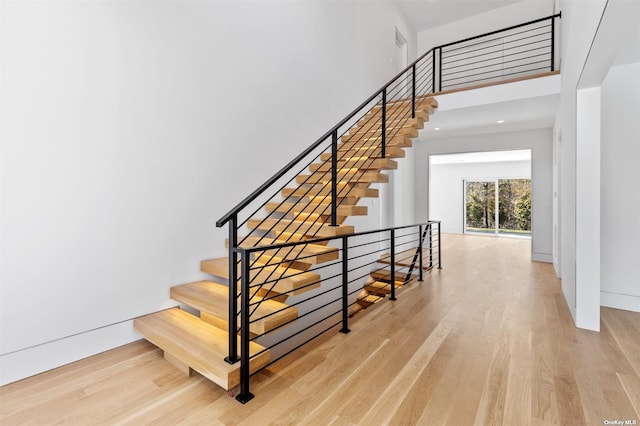 stairway featuring a high ceiling, baseboards, and wood finished floors