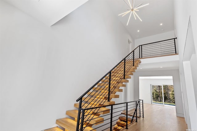 stairway featuring recessed lighting, wood finished floors, a notable chandelier, and a towering ceiling