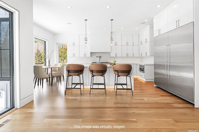 kitchen with light wood-type flooring, a kitchen bar, visible vents, built in fridge, and white cabinetry