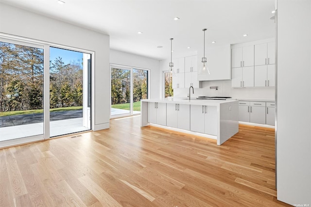 kitchen with light wood-style flooring, a kitchen island with sink, and white cabinets