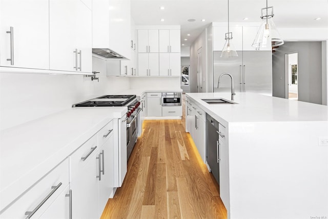 kitchen with wall chimney range hood, light wood-style flooring, white cabinets, stainless steel appliances, and a sink