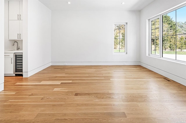 empty room with wine cooler, plenty of natural light, wet bar, and light wood finished floors