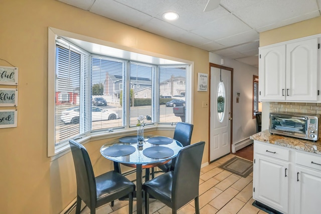 dining area with a toaster, baseboard heating, baseboards, and a drop ceiling