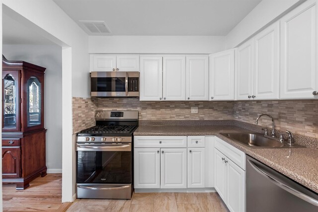 kitchen with visible vents, a sink, stainless steel appliances, white cabinetry, and tasteful backsplash