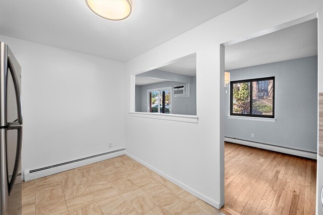 empty room featuring a baseboard heating unit, baseboards, and a healthy amount of sunlight