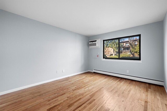 unfurnished room with a wall mounted air conditioner, a baseboard heating unit, baseboards, and wood finished floors