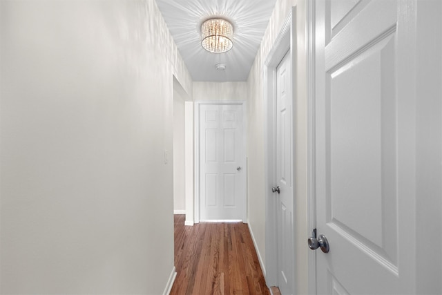 hallway with an inviting chandelier, dark wood-style floors, and baseboards