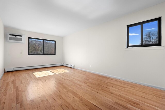 spare room with light wood-type flooring, baseboards, baseboard heating, and an AC wall unit