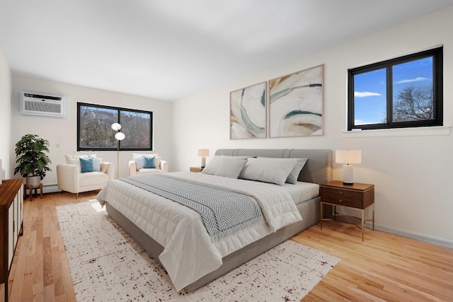 bedroom featuring a baseboard radiator, multiple windows, light wood-style flooring, and a wall mounted AC