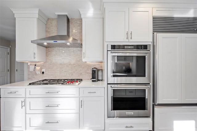 kitchen with light countertops, decorative backsplash, white cabinets, stainless steel appliances, and wall chimney exhaust hood