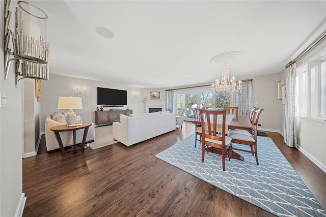 dining room with a chandelier, baseboards, a fireplace, and dark wood-style flooring