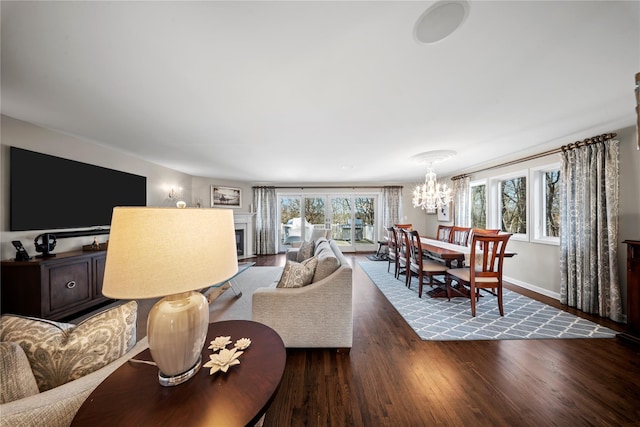 living room with a chandelier, a fireplace, baseboards, and wood finished floors