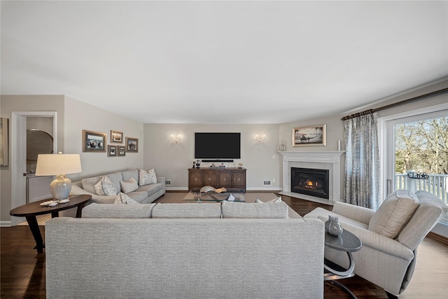 living area with baseboards, a fireplace with flush hearth, and dark wood-type flooring