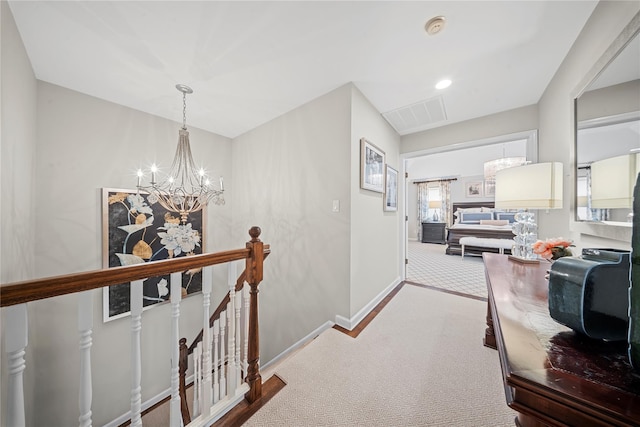 hallway with visible vents, an upstairs landing, a notable chandelier, carpet flooring, and baseboards