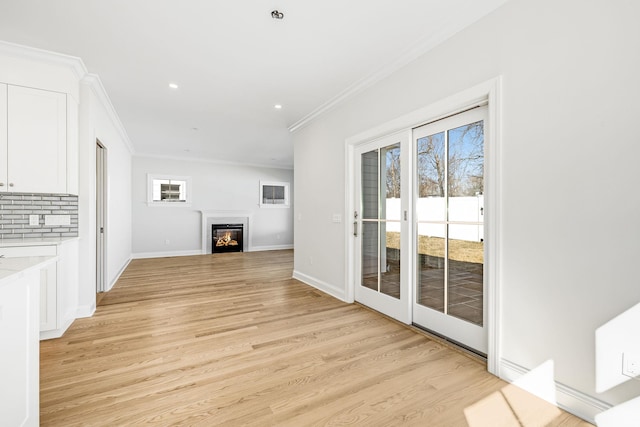 unfurnished living room with a glass covered fireplace, light wood-type flooring, baseboards, and ornamental molding