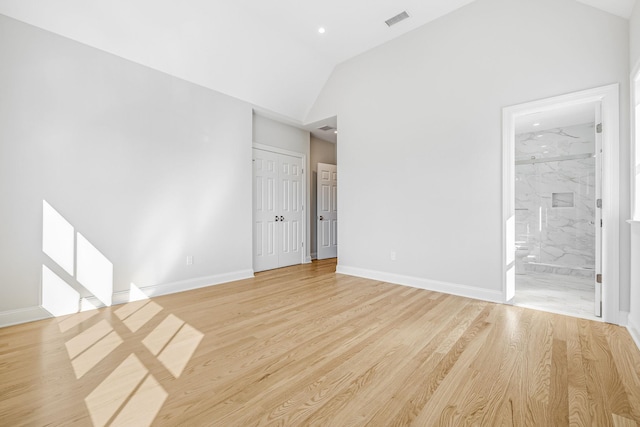 empty room with lofted ceiling, light wood-style floors, visible vents, and baseboards