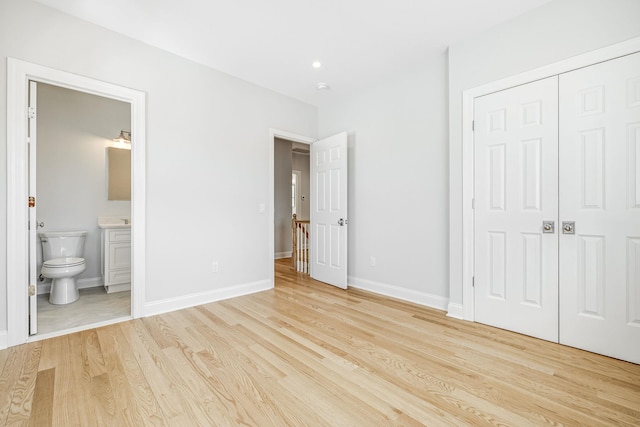 unfurnished bedroom featuring a closet, ensuite bathroom, baseboards, and light wood finished floors