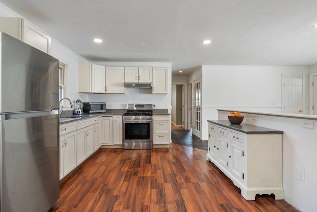 kitchen featuring under cabinet range hood, a sink, dark countertops, stainless steel appliances, and dark wood-style flooring