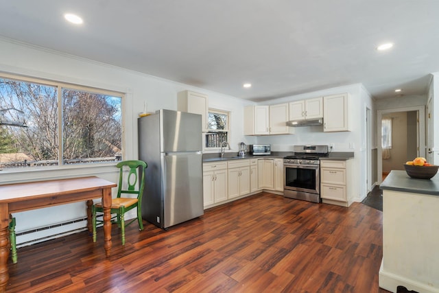 kitchen featuring under cabinet range hood, dark countertops, dark wood finished floors, stainless steel appliances, and baseboard heating