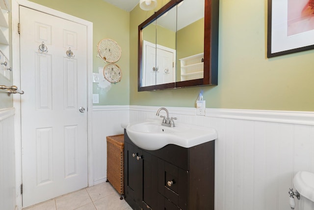 half bath with vanity, tile patterned floors, toilet, and a wainscoted wall