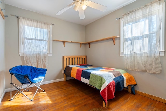 bedroom featuring a ceiling fan, multiple windows, wood finished floors, and baseboards