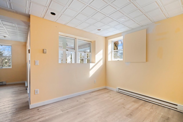 spare room with a baseboard heating unit, baseboards, plenty of natural light, and wood finished floors