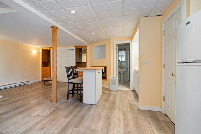 kitchen with a baseboard heating unit, a kitchen bar, light wood-style floors, and freestanding refrigerator