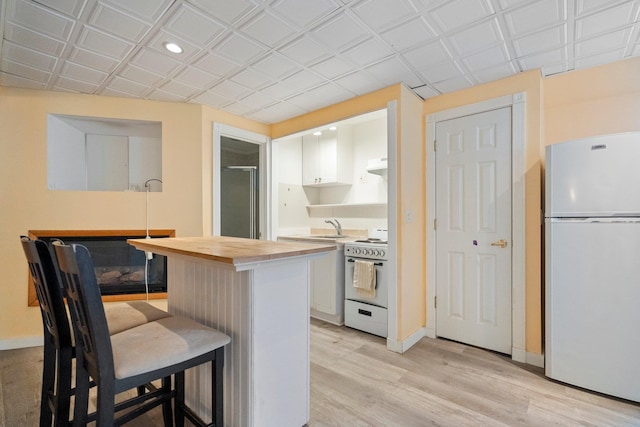 kitchen with white cabinetry, white appliances, a kitchen bar, and wood counters