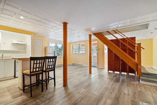 below grade area with stairway, baseboards, a baseboard radiator, a sink, and light wood-style floors