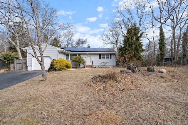 single story home with driveway, entry steps, roof mounted solar panels, fence, and a garage