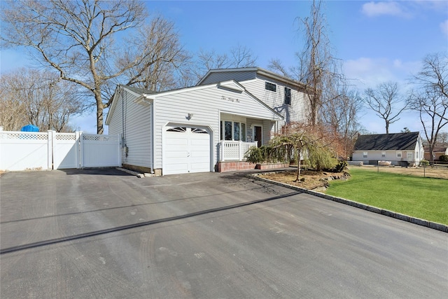 view of side of home with a gate, aphalt driveway, fence, a yard, and a garage